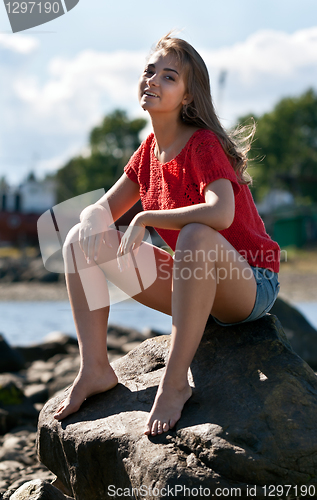 Image of girl in a red sweater sits on a rock