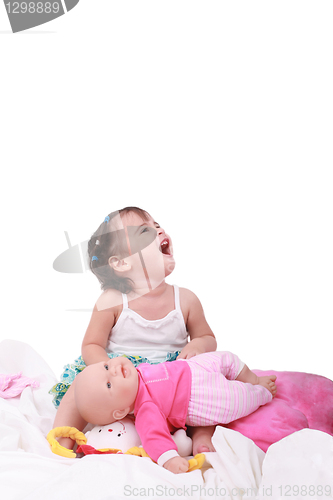 Image of happy little baby girl sitting in the bed with her dolls