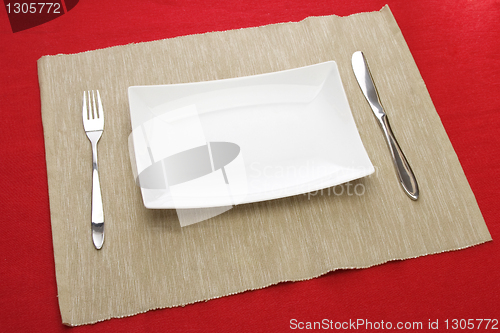 Image of white plate fork and knife on red table