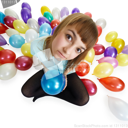 Image of Young woman sitting on floor among balloons