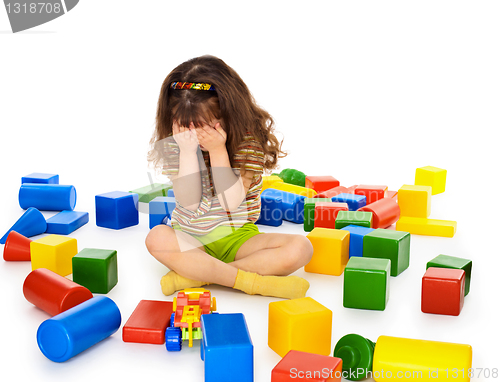 Image of Little girl sitting on white among toys and crying