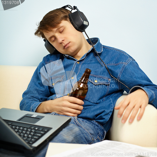 Image of Man fell asleep at home on couch with a beer