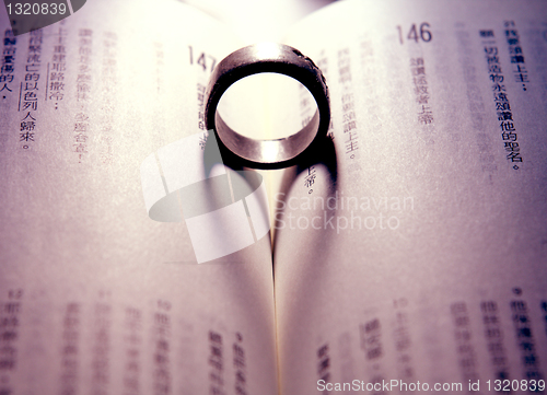 Image of ring casts the shadow of a heart against the pages of a book 