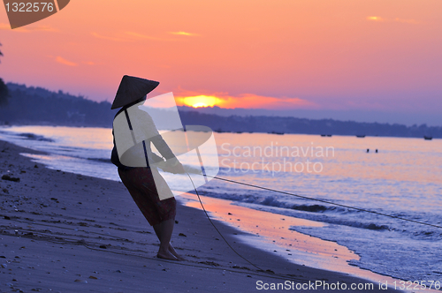 Image of Silhouette of a fisherman on beach at sunrise