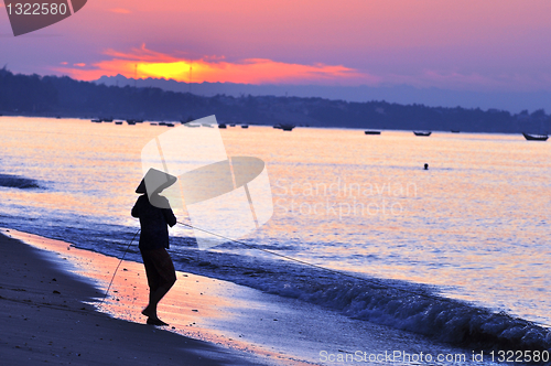 Image of Silhouette of a fisherman on beach at sunrise