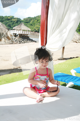 Image of baby girl in sunglasses on the beach playing getting prepared fo