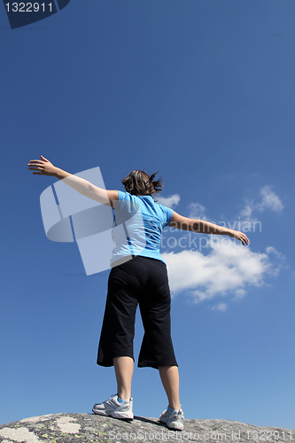 Image of young woman with arms wide open against blue sky