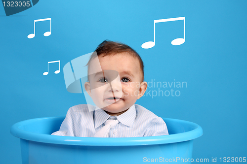 Image of baby on a blue bucket, studio shoot, listen some musical notes