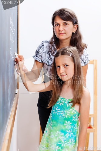 Image of Girl writing on chalkboard with teacher's help