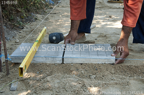 Image of Worker puts sidewalk tiles