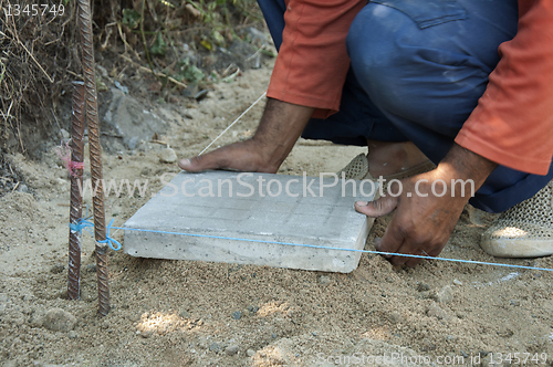 Image of Worker puts sidewalk tiles