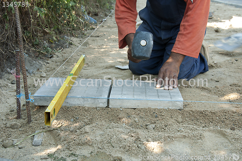 Image of Worker puts sidewalk tiles