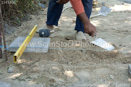 Image of Worker puts sidewalk tiles