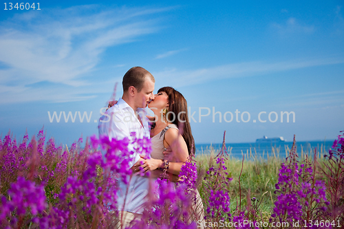 Image of Romantic kiss among purple flowers near blue sea