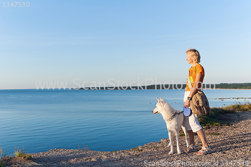 Image of The woman with a dog costs on edge of breakage at the sea