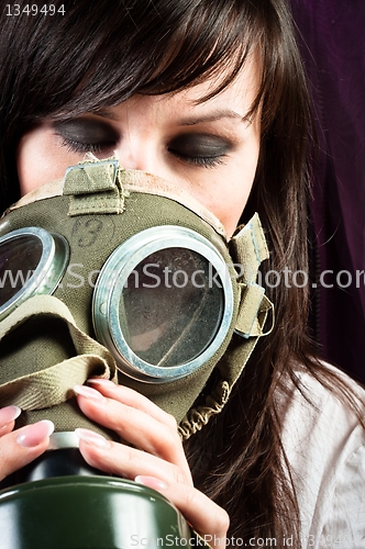 Image of Beautiful girl is holding an old gasmask against dark background