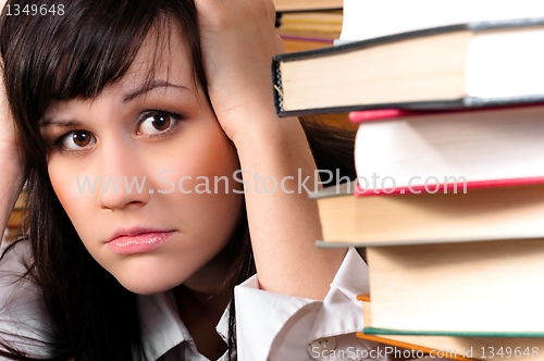 Image of Young student girl holding her head behind a lot of books