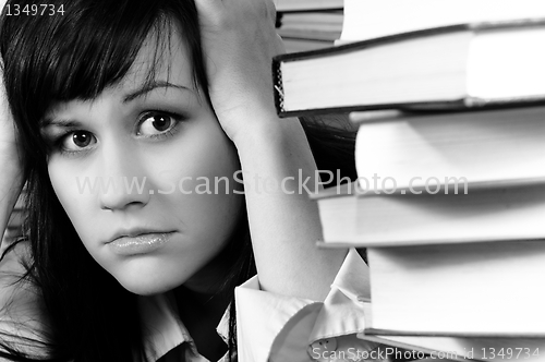 Image of Young student girl holding her head behind a lot of books