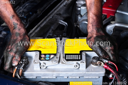 Image of Engineer with oil on his hands holding a car battery tight