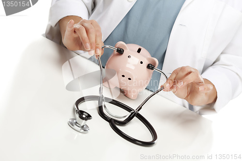 Image of Doctor Holds Stethoscope to Ears of Pink Piggy Bank