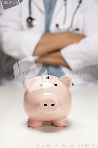 Image of Doctor with Folded Arms Behind Piggy Bank