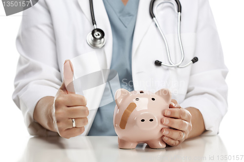 Image of Doctor with Thumbs Up Holds Hand to Bandaged Piggy Bank