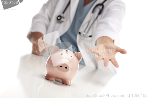Image of Demanding Doctor Reaches Palm Out Behind Piggy Bank