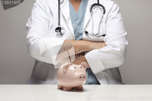 Image of Doctor with Folded Arms Behind Piggy Bank