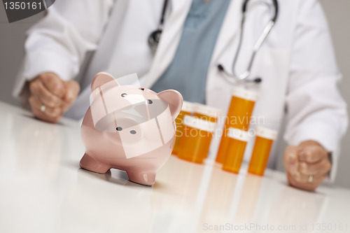 Image of Doctor with Fists on Table Behind Bottle and Piggy Bank