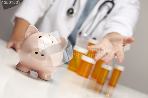 Image of Doctor Reaches Palm Out Behind Medicine Bottles and Piggy Bank