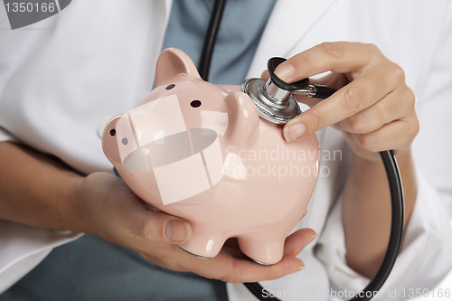 Image of Doctor Holding Stethoscope to Piggy Bank