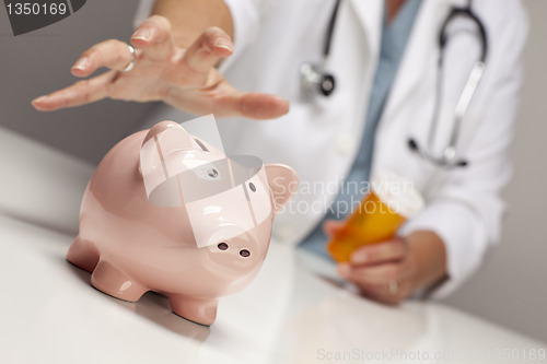 Image of Doctor with Medicine Bottles Reaches for Piggy Bank.