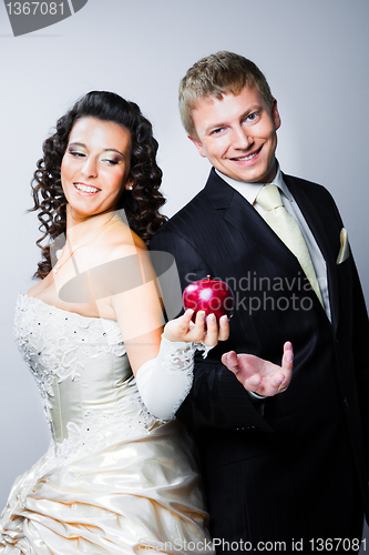 Image of just married bride tempting smiling groom by red apple