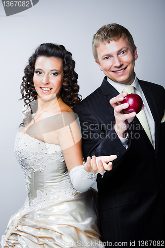 Image of groom taking red apple from young beautiful bride