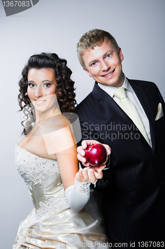 Image of groom taking red apple from young beautiful bride