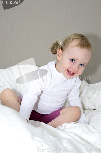 Image of little girl sitting on a bed and smiling