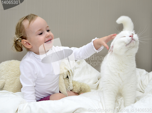 Image of little girl sitting on the bed and plays with a cat