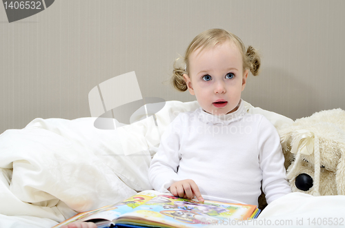 Image of little girl sitting on the bed and reading a book