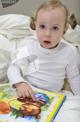 Image of little girl sitting on the bed and reading a book