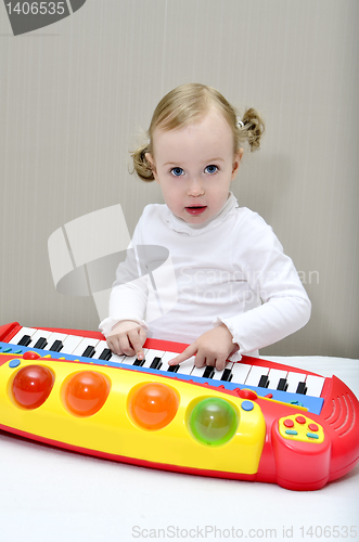 Image of little girl sitting on the bed and plays on a children's keyboard