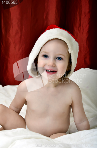 Image of little girl in a Christmas red hat sitting on a bed