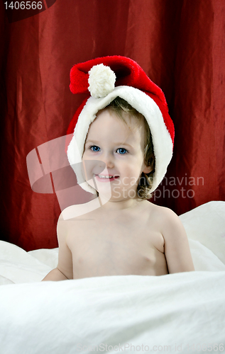 Image of little girl in a Christmas red hat sitting on a bed