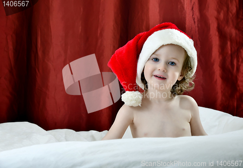 Image of little girl in a Christmas red hat sitting on a bed