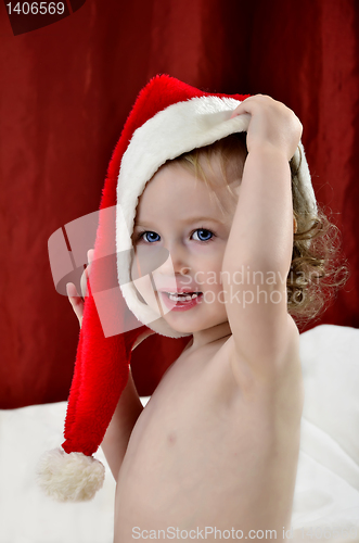 Image of little girl in a Christmas red hat sitting on a bed