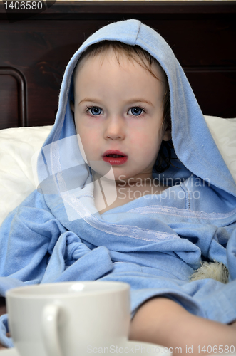 Image of little girl in a blue robe resting on the bed after a shower with a cup of tea