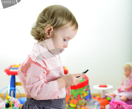 Image of little girl standing with mobile phone in room with toys