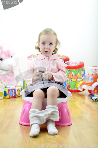 Image of little girl sitting on the potty with a remote control (or mobile phone) in hand