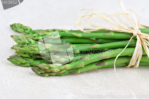 Image of Fresh organic asparagus bunch tied with raffia on a tile counter