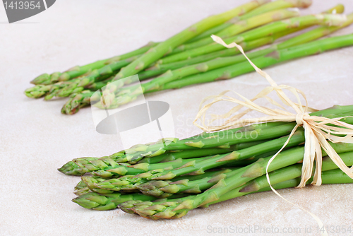 Image of Two bunches of fresh asparagus on tile counter top.