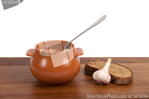 Image of Borsch in clay pot with bread and garlic on wooden table